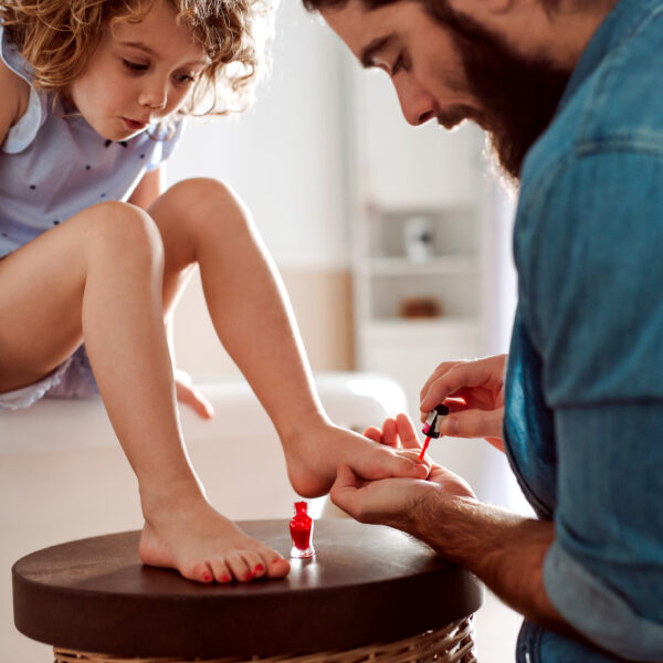 A young father painting small daughter's nails in a bathroom at home.